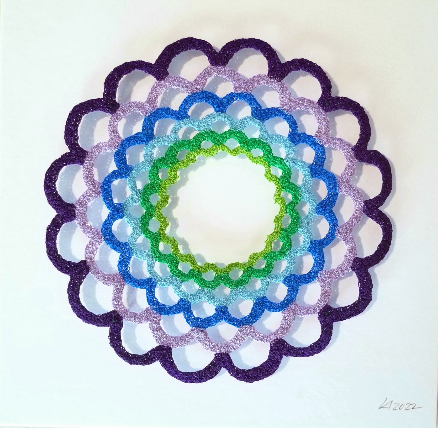 Decorative circular design with concentric rings in purple, blue, green, and white on a white background.