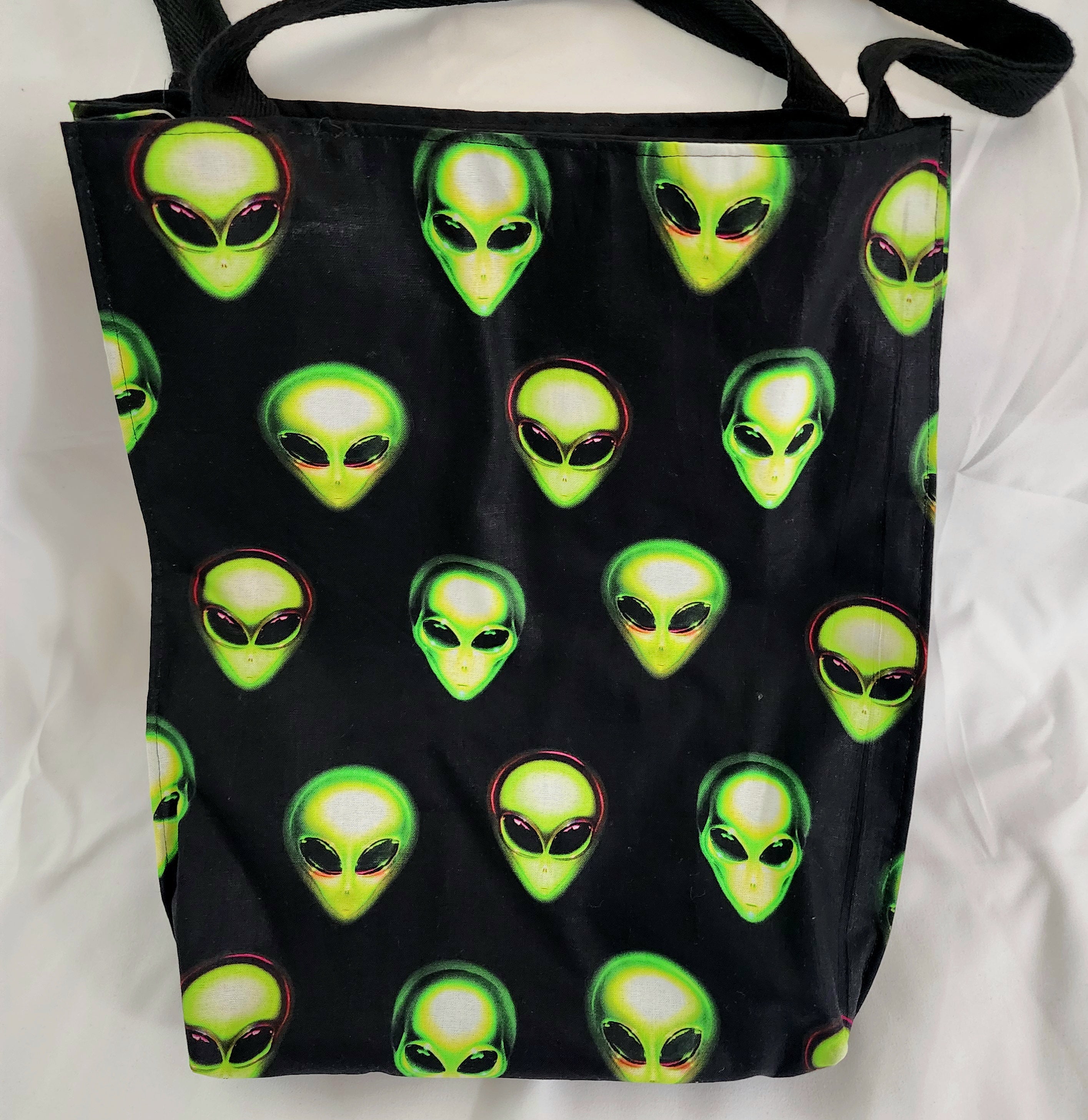 Black tote bag with green alien heads pattern on a white background