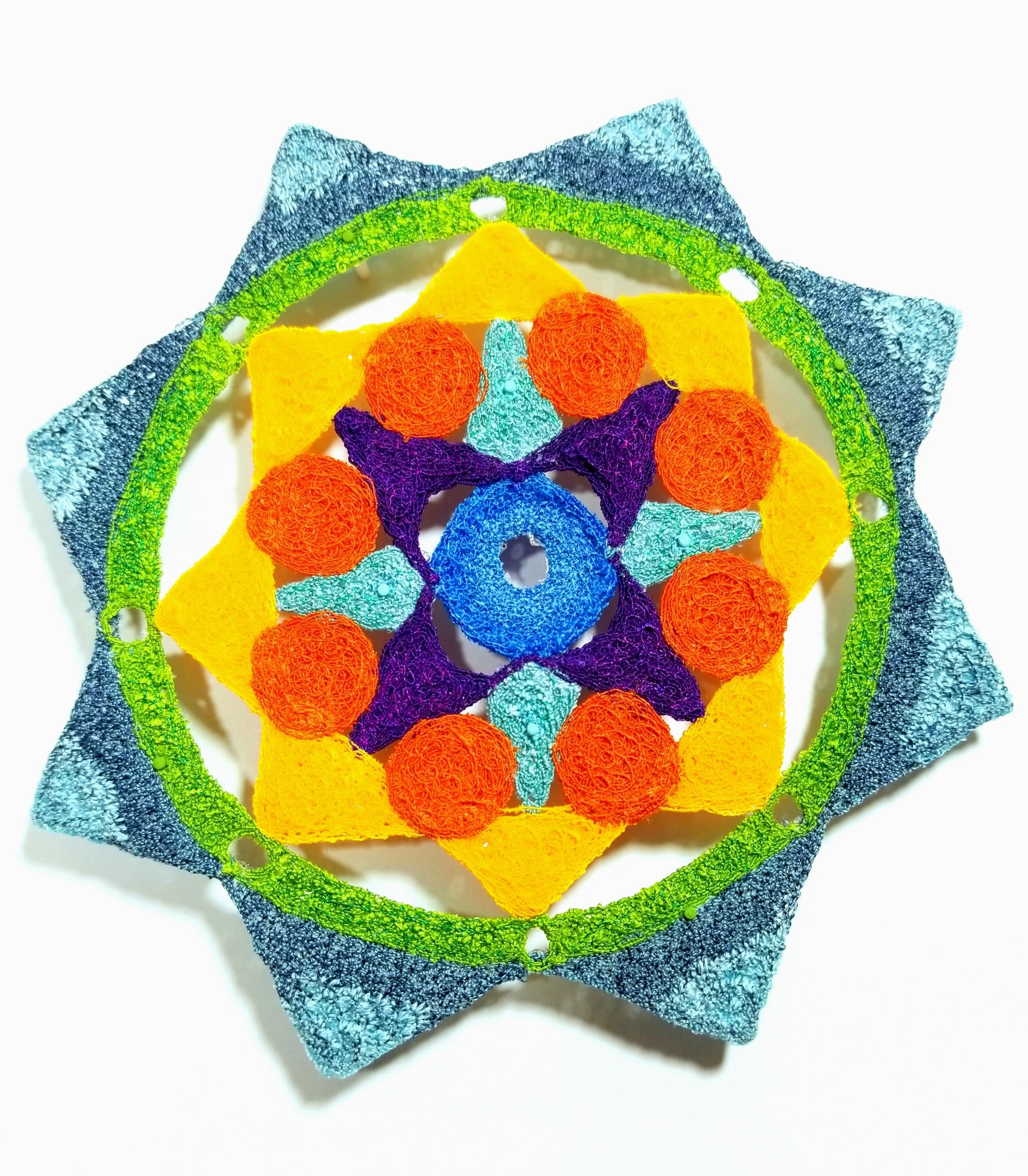 Colorful crocheted star-shaped object with a blue center on a white background
