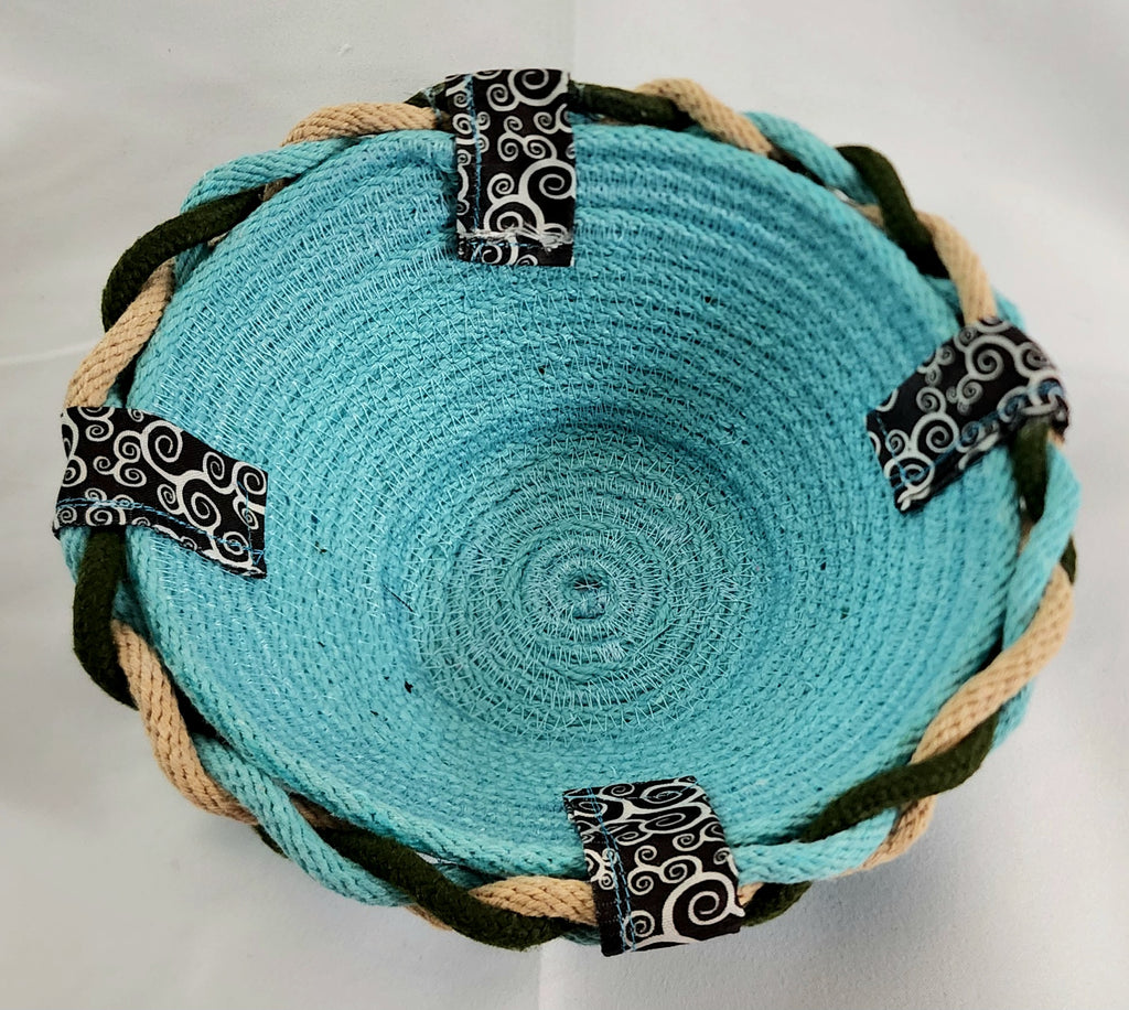 Turquoise woven bowl with black and white patterned straps on a white background