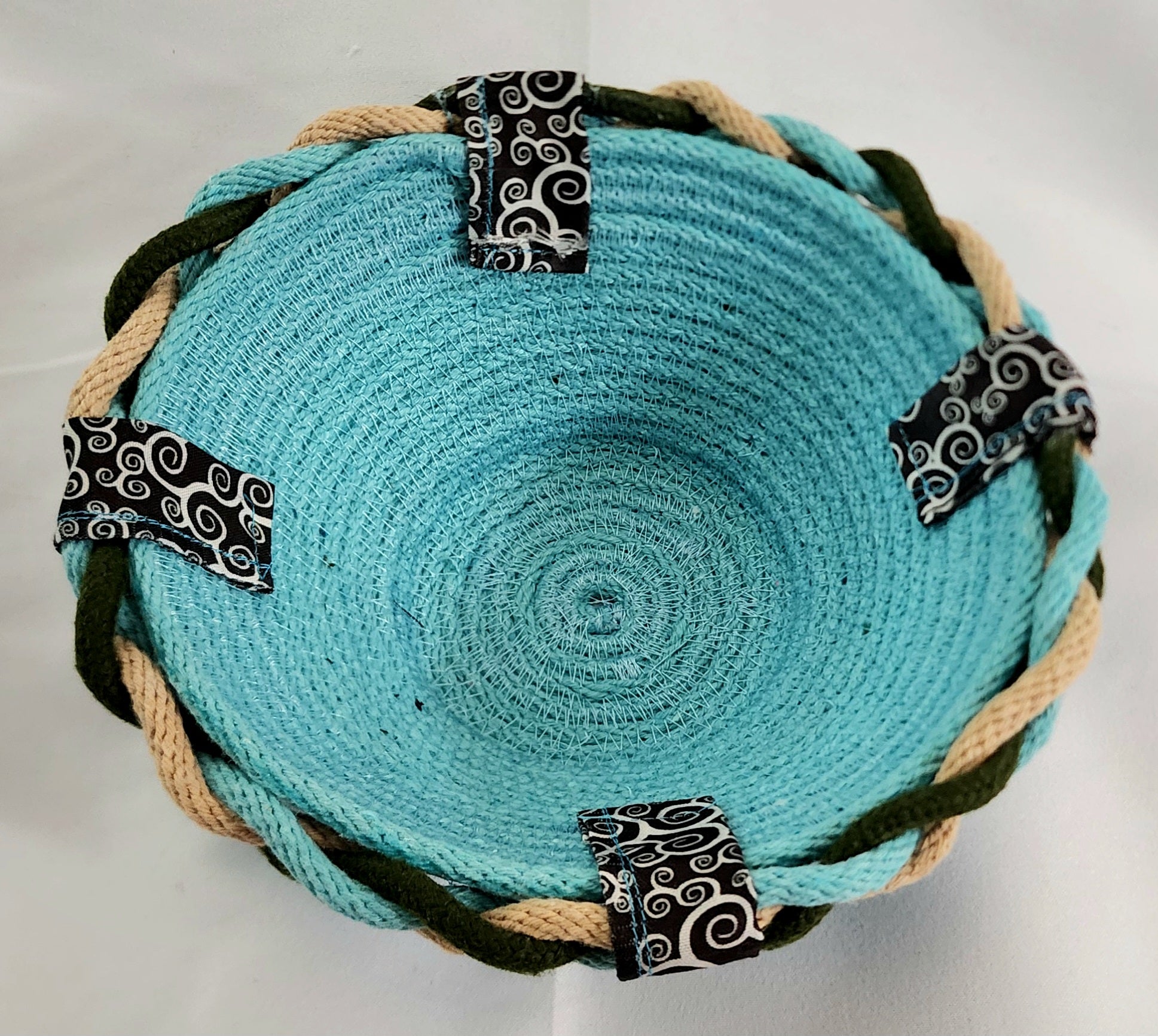 Turquoise woven bowl with black and white patterned straps on a white background